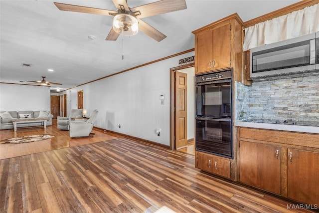 kitchen featuring brown cabinetry, wood finished floors, black appliances, light countertops, and crown molding