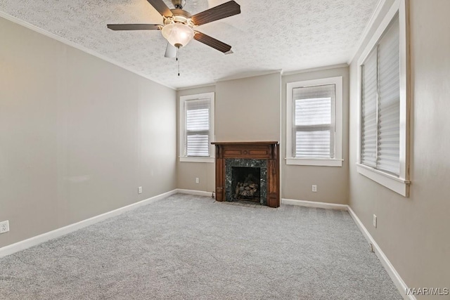 unfurnished living room with baseboards, carpet floors, a high end fireplace, ceiling fan, and a textured ceiling