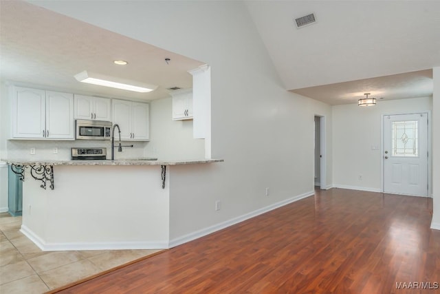 kitchen featuring stainless steel microwave, visible vents, a peninsula, white cabinets, and range