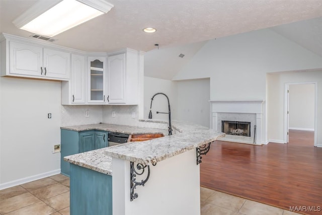 kitchen featuring light tile patterned floors, light stone countertops, a peninsula, lofted ceiling, and white cabinets