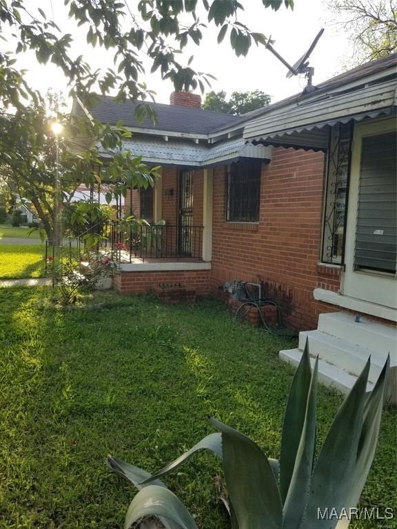 view of property exterior with a chimney, a lawn, a porch, and brick siding