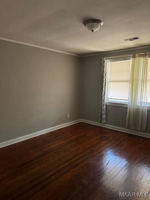 empty room featuring dark wood finished floors, visible vents, baseboards, and ornamental molding