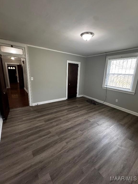 unfurnished room featuring dark wood-style flooring, ornamental molding, and baseboards
