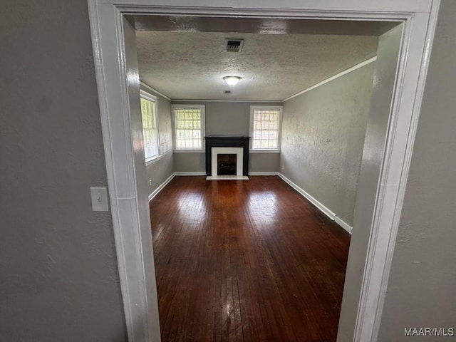 unfurnished living room featuring ornamental molding, a fireplace with flush hearth, a textured wall, a textured ceiling, and hardwood / wood-style flooring