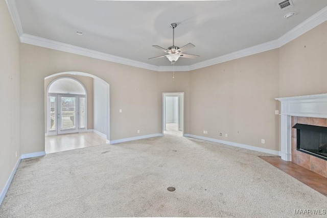 unfurnished living room featuring baseboards, a tiled fireplace, ornamental molding, light carpet, and arched walkways