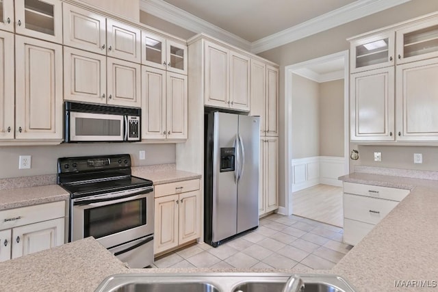 kitchen with light countertops, ornamental molding, light tile patterned floors, wainscoting, and appliances with stainless steel finishes