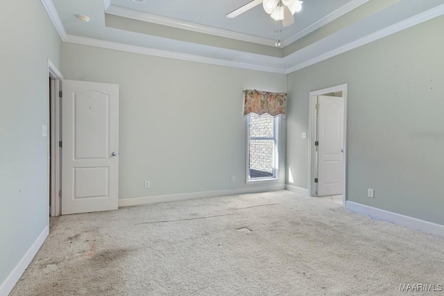 carpeted spare room featuring a raised ceiling, crown molding, baseboards, and ceiling fan