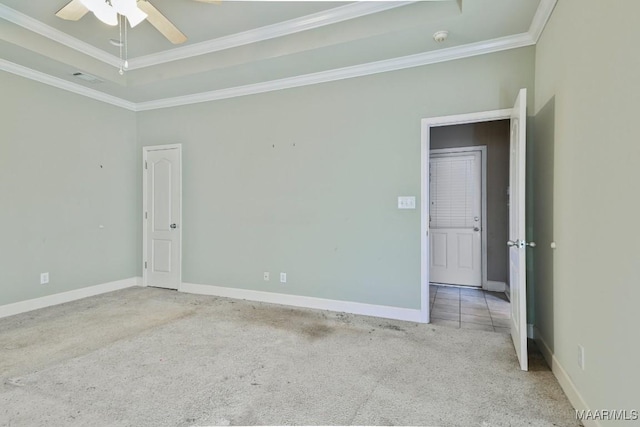 empty room featuring a raised ceiling, a ceiling fan, carpet flooring, crown molding, and baseboards