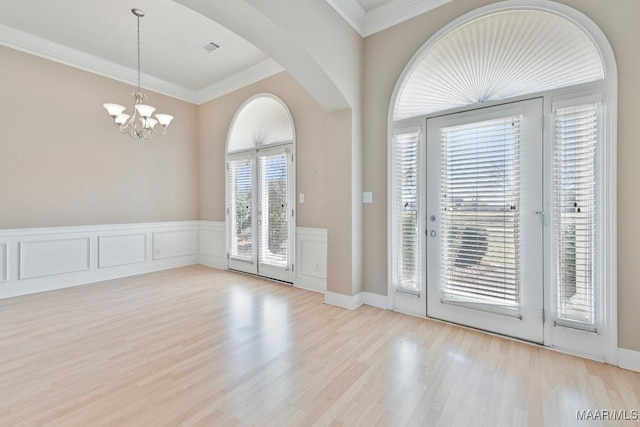 foyer with visible vents, ornamental molding, wainscoting, wood finished floors, and a decorative wall