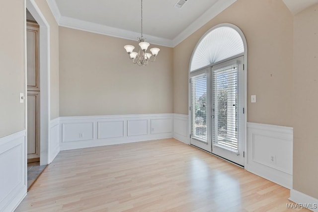 spare room featuring a notable chandelier, wainscoting, crown molding, and light wood finished floors