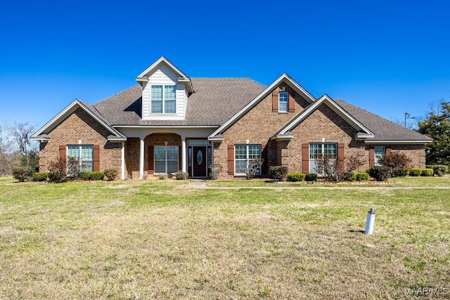 view of front of home with brick siding, a front lawn, and roof with shingles