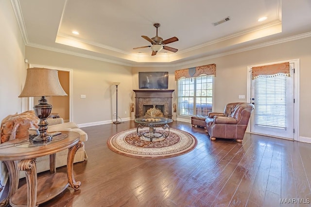 living area featuring visible vents, a fireplace with raised hearth, ornamental molding, dark wood-style floors, and a raised ceiling