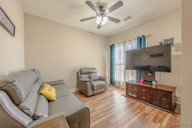 living room featuring light wood-type flooring, visible vents, baseboards, and a ceiling fan