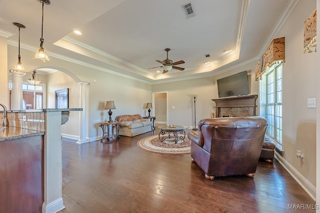 living room with arched walkways, dark wood-type flooring, a tray ceiling, and ornamental molding