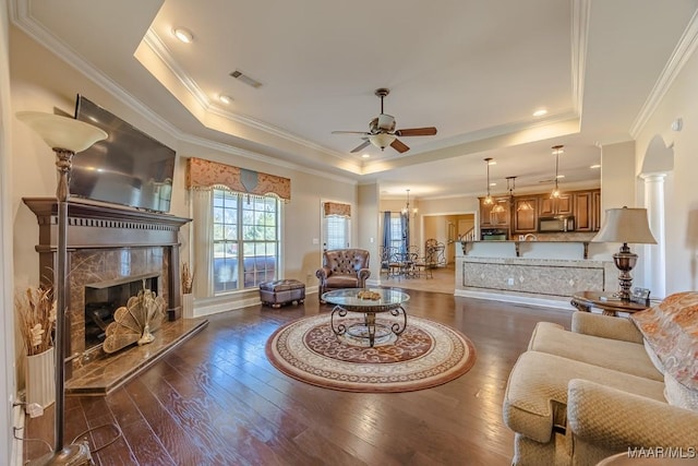 living area featuring visible vents, ceiling fan with notable chandelier, a tray ceiling, a high end fireplace, and wood-type flooring