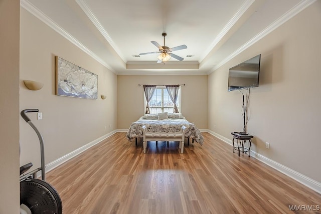 bedroom featuring a tray ceiling, crown molding, wood finished floors, and baseboards