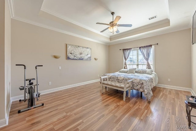 bedroom featuring visible vents, crown molding, baseboards, light wood-type flooring, and a tray ceiling