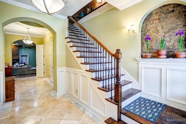 stairs with tile patterned floors, a decorative wall, wainscoting, and crown molding