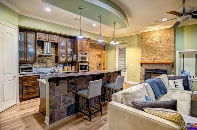 bar featuring light wood-style flooring, ornamental molding, wall chimney range hood, decorative backsplash, and a brick fireplace