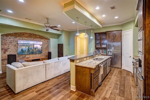 kitchen with an island with sink, stainless steel fridge with ice dispenser, light wood-style floors, and a sink