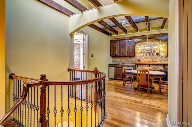 interior space featuring baseboards, light wood-style flooring, arched walkways, beamed ceiling, and backsplash