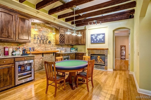 rec room with beam ceiling, light wood-style floors, beverage cooler, and a tiled fireplace