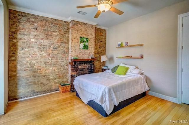 bedroom featuring wood finished floors, visible vents, brick wall, baseboards, and ornamental molding