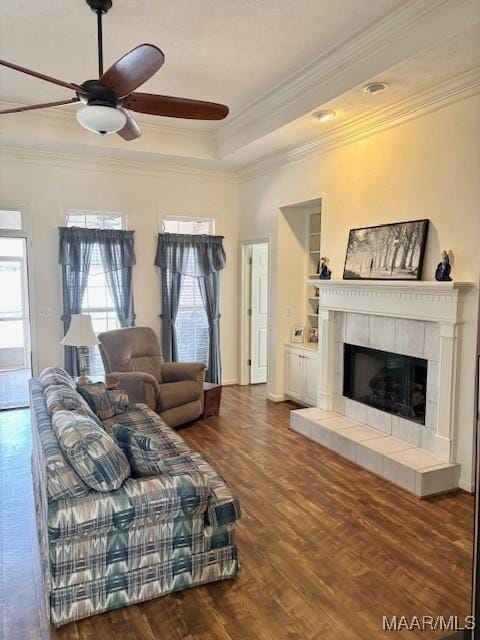 living area featuring a tiled fireplace, dark wood-type flooring, a tray ceiling, and ornamental molding