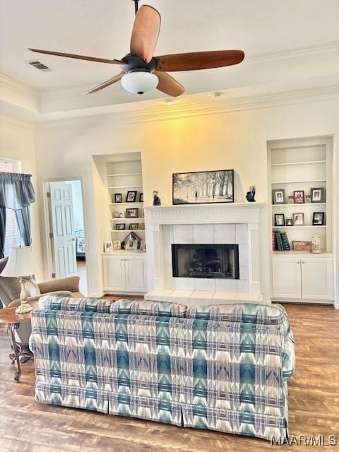 living room with visible vents, built in shelves, crown molding, and a tile fireplace