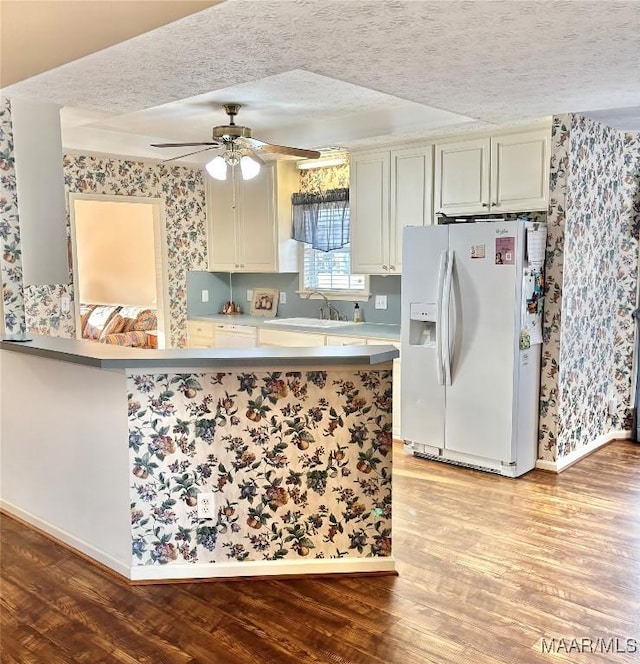 kitchen featuring wallpapered walls, a sink, light wood-style floors, white fridge with ice dispenser, and a textured ceiling