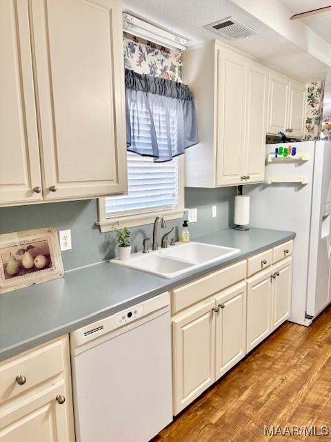 kitchen with visible vents, light wood-style flooring, a sink, white appliances, and light countertops