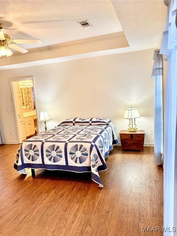 bedroom with a raised ceiling, wood finished floors, visible vents, and ornamental molding