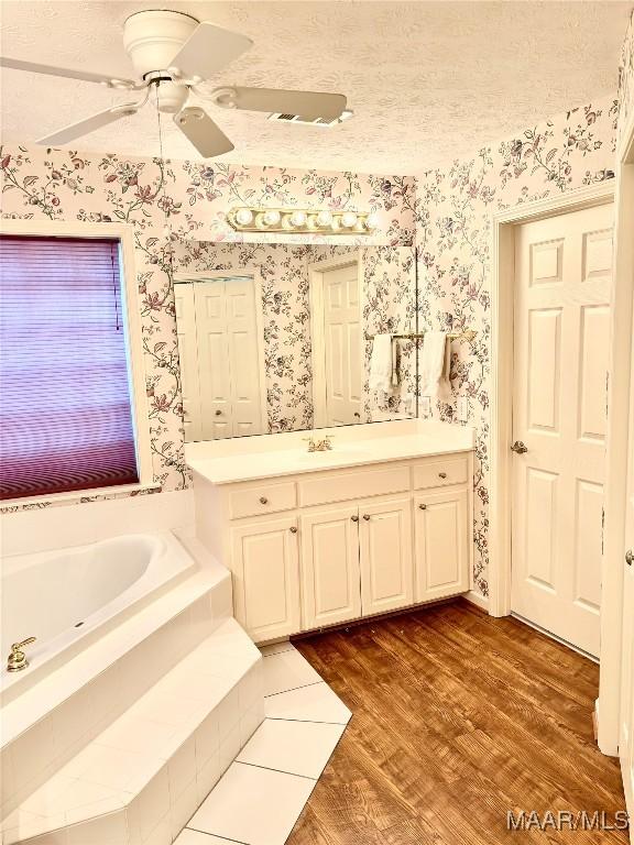 bathroom with vanity, wood finished floors, wallpapered walls, a textured ceiling, and a bath