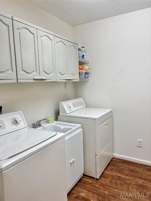 clothes washing area featuring dark wood-type flooring, independent washer and dryer, a textured ceiling, cabinet space, and baseboards