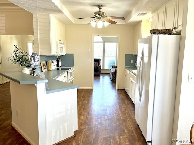 kitchen featuring white appliances, a raised ceiling, ceiling fan, dark wood-style flooring, and a peninsula