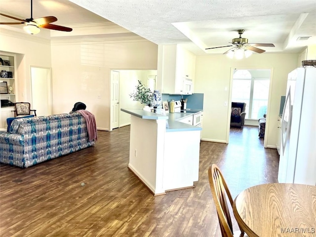 kitchen featuring ceiling fan, white appliances, a raised ceiling, dark wood-style floors, and a peninsula