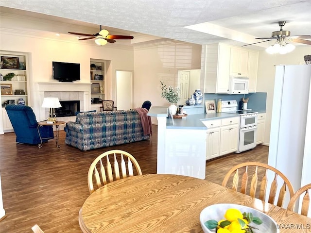dining area featuring a ceiling fan, wood finished floors, built in shelves, a tiled fireplace, and ornamental molding