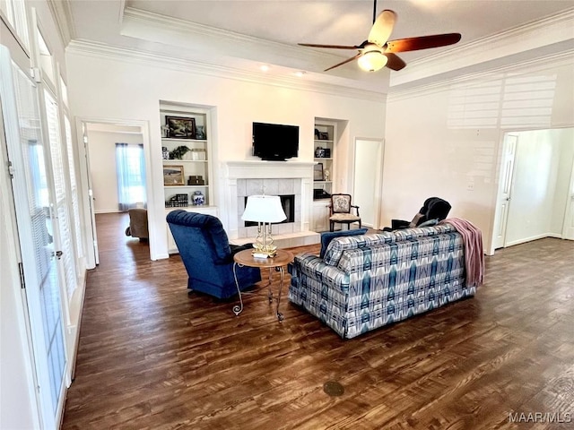 living area with a fireplace, a tray ceiling, built in features, and crown molding