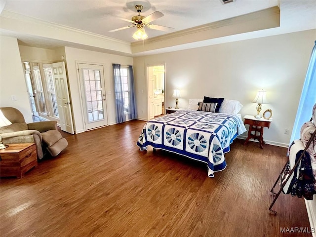 bedroom featuring a raised ceiling, crown molding, wood finished floors, baseboards, and a ceiling fan