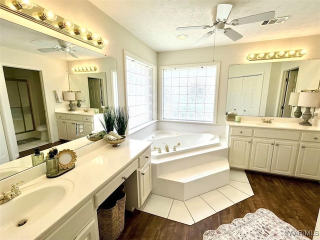 bathroom featuring a ceiling fan, a bath, a textured ceiling, two vanities, and wood finished floors