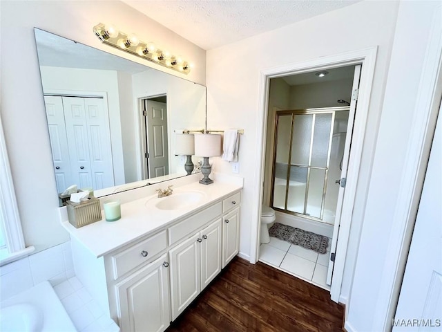 full bathroom with a shower stall, toilet, vanity, wood finished floors, and a textured ceiling