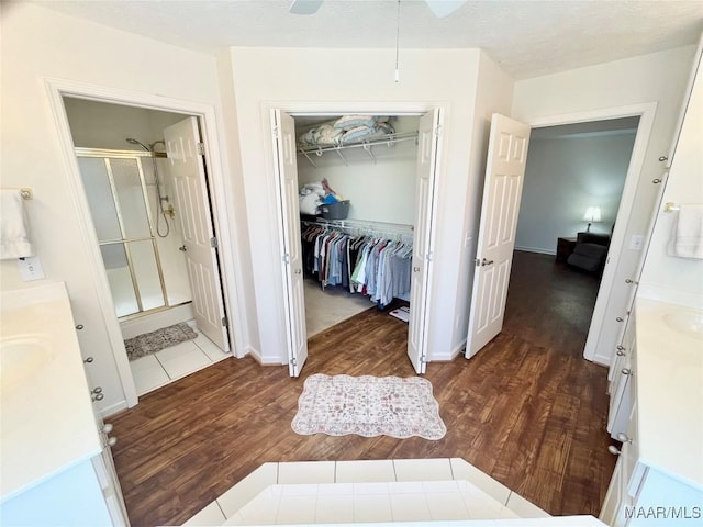 bathroom featuring a stall shower, vanity, wood finished floors, a spacious closet, and ceiling fan