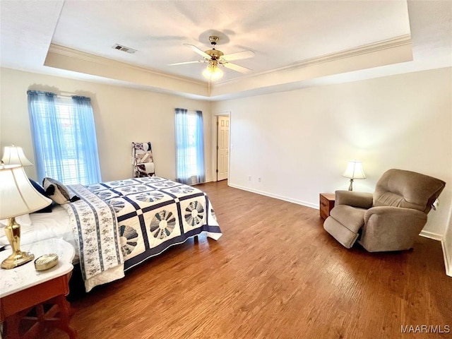bedroom featuring a raised ceiling, crown molding, wood finished floors, baseboards, and a ceiling fan