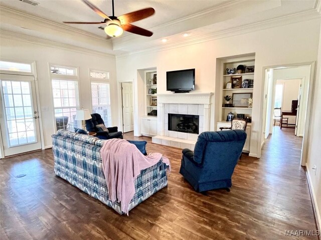living room featuring ornamental molding, a ceiling fan, built in features, dark wood finished floors, and a tray ceiling