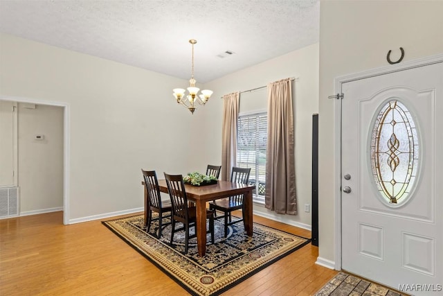 dining area featuring light wood-style flooring, a notable chandelier, baseboards, and a textured ceiling