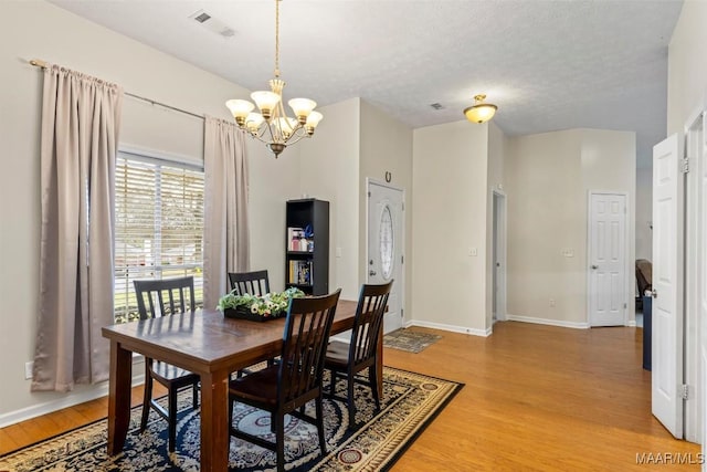 dining area featuring light wood finished floors, visible vents, baseboards, and a notable chandelier