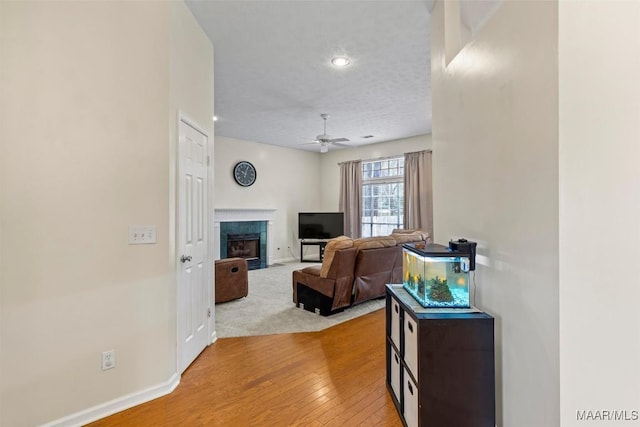 living room featuring a textured ceiling, wood finished floors, a fireplace, baseboards, and ceiling fan