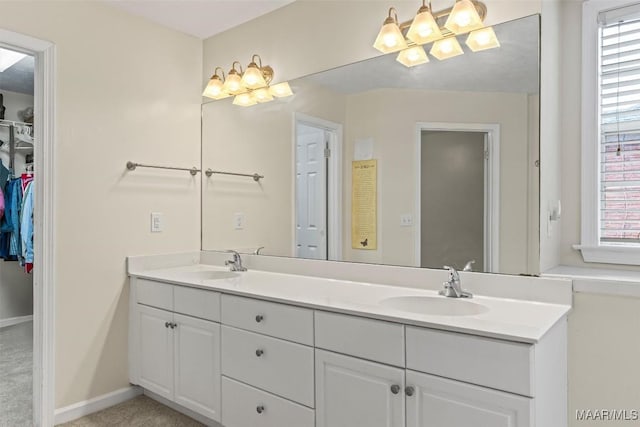 bathroom featuring a walk in closet, double vanity, baseboards, and a sink