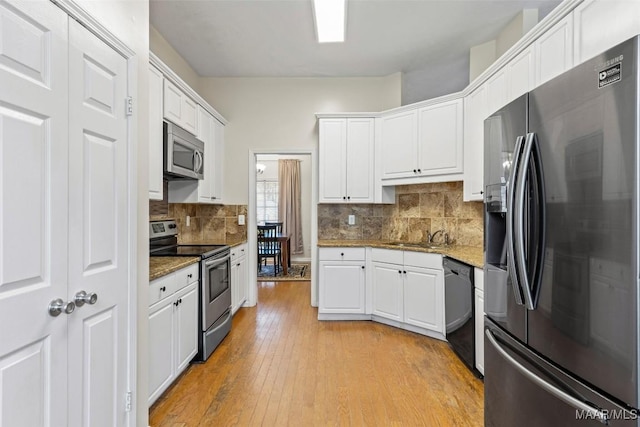 kitchen with white cabinets, light wood finished floors, tasteful backsplash, and appliances with stainless steel finishes