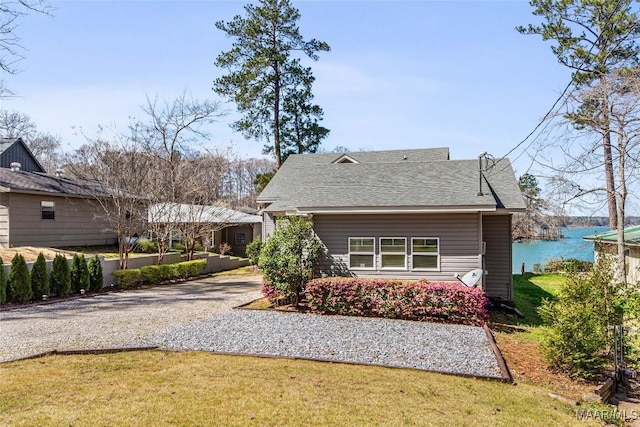 view of front of home with driveway, a shingled roof, a front yard, and a water view